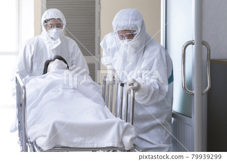 asian male nurse and doctor wearing ppe suit and face mask pushing stretcher gurney bed with seriously infected coronavirus or covid-19 patient towards quarantine room in hospital with copy space. 79939299