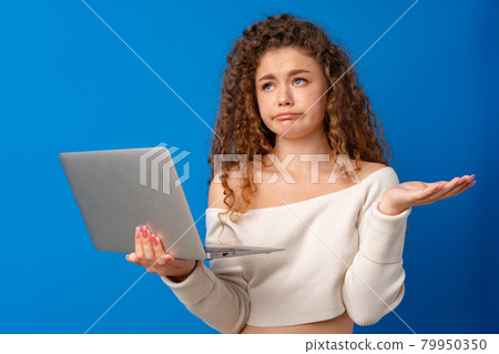 Young curly-haired woman holding laptop against blue background 79950350