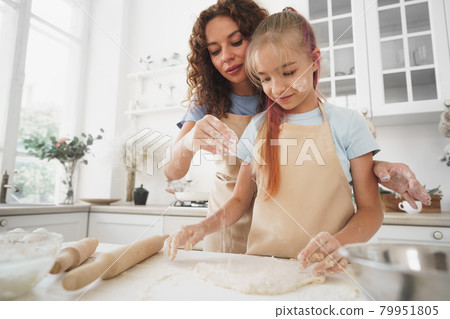Teen girl helping her mom to cook dough in their kitchen at home 79951805