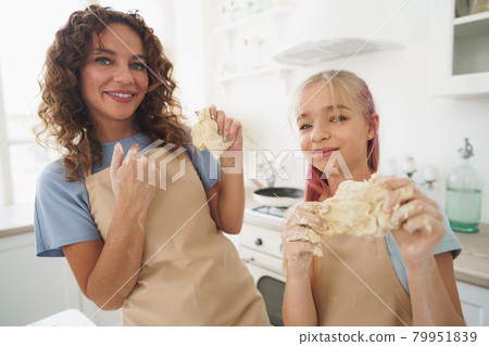 Teen girl helping her mom to cook dough in their kitchen at home Teen girl helping her mom to cook dough in their kitchen at home 79951839