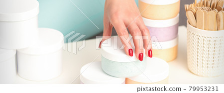 Beautician's hand takes jar with cosmetics from table offering and selling cosmetic products, moisturizing cream, wax paste. 79953231