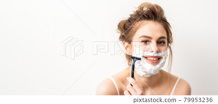 Portrait of beautiful young smiling caucasian woman shaves face with razor on white background. 79953236