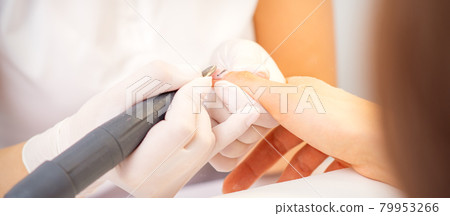 Closeup of manicure master in white gloves applying an electric nail file drill to remove the nail polish in the beauty salon. Closeup of manicure master in white gloves applying an electric nail file drill to remove the nail polish in the beauty salon. 79953266