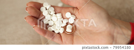 Many white pills and wedding ring lying on womans hand closeup 79954180