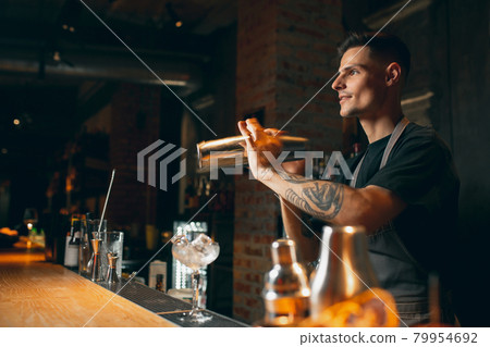 Shaking, mixing. One professional bartender shaking an alcohol drink in cocktail shaker enjoying his job. Side view Shaking, mixing. One professional bartender shaking an alcohol drink in cocktail shaker enjoying his job. Side view 79954692
