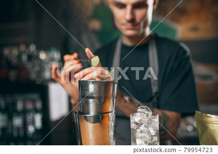 Young caucasian guy, professional bartender in apron mixing cocktails in pub or cafe. 79954723