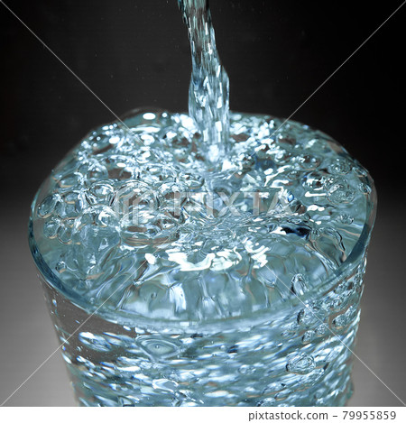 Water runs with bubbles into a glass that overflows against a dark background 79955859
