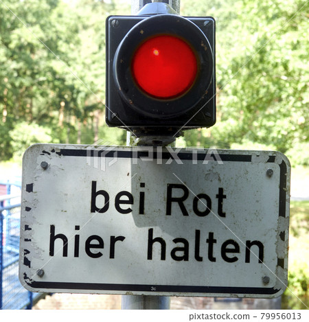 Red shining light above a sign with the German inscription: stop here at red! Red shining light above a sign with the German inscription: stop here at red! 79956013