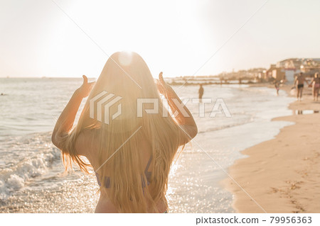 Young girl straightens her hair with her hands against the backdrop of the sea beach and sunset Young girl straightens her hair with her hands against the backdrop of the sea beach and sunset 79956363