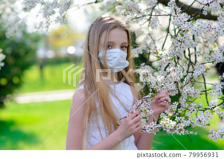 Teenager girl in medical mask in spring flowering garden. Teenager girl in medical mask in spring flowering garden. 79956931