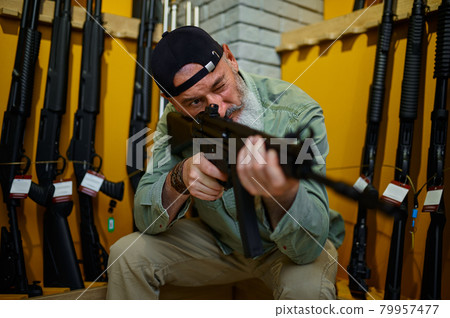 Bearded man checks the rifle scope in gun store Bearded man checks the rifle scope in gun store 79957477