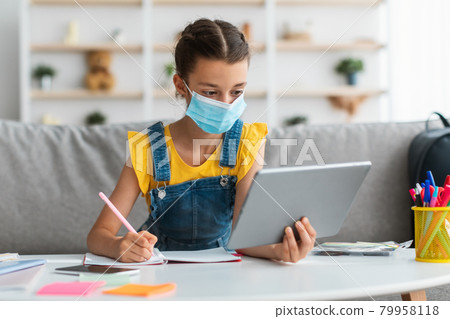Schoolgirl in medical mask studying at home with digital tablet Schoolgirl in medical mask studying at home with digital tablet 79958118