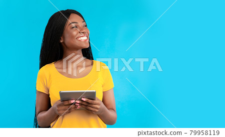 Black woman using digital tablet looking aside over blue background Black woman using digital tablet looking aside over blue background 79958119