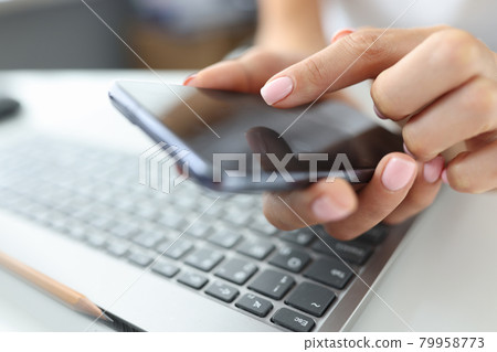 Girl presses finger on screen of smartphone on table is laptop Girl presses finger on screen of smartphone on table is laptop 79958773