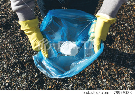A man volunteer collects garbage on a dirty beach. The concept of waste recycling, environmental cleaning A man volunteer collects garbage on a dirty beach. The concept of waste recycling, environmental cleaning 79959328