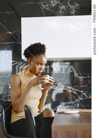 African girl drinks coffee in kitchen by windows 79960198