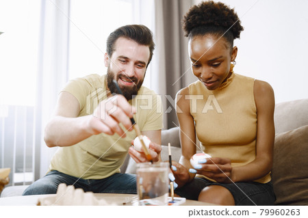 African woman and caucasian man paint easter eggs African woman and caucasian man paint easter eggs 79960263