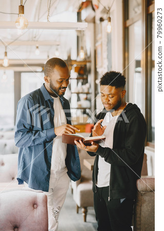 Two men talking in a cafe, holding a notebook. 79960273