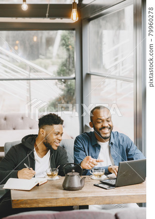 Two men sitting in a cafe and working behind a laptop and drink a tea. Two men sitting in a cafe and working behind a laptop and drink a tea. 79960278