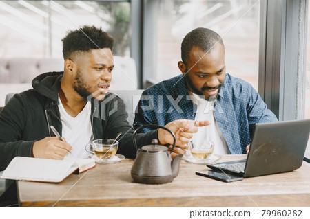 Two men sitting in a cafe and working behind a laptop and drink a tea. 79960282