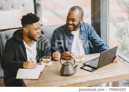 Two men sitting in a cafe and working behind a laptop and drink a tea. 79960285