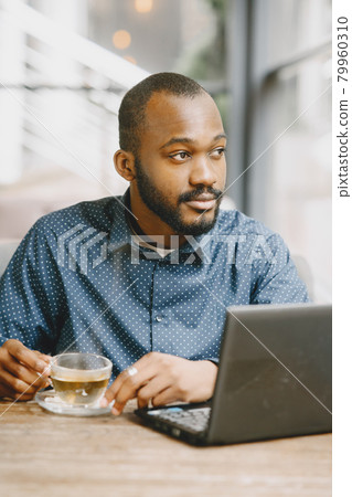 Man sitting in a cafe and working behind a laptop and drink a tea. 79960310