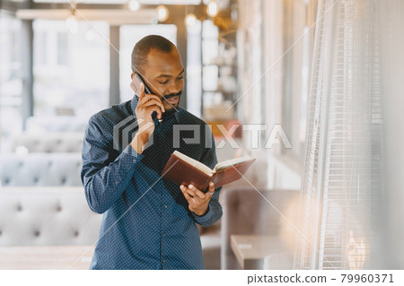 Man sitting in a cafe and talking on the phone, holding a notebook. 79960371