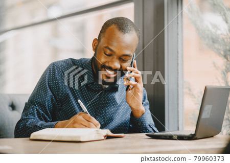 Man sitting in a cafe and working behind a laptop, writing in a notebook. 79960373