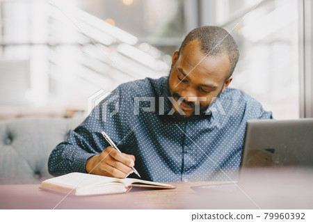 Man working behind a laptop writing in a notebook, cafe Man working behind a laptop writing in a notebook, cafe 79960392