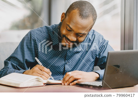 Man sitting in a cafe and working behind a laptop, writing in a notebook. Man sitting in a cafe and working behind a laptop, writing in a notebook. 79960417