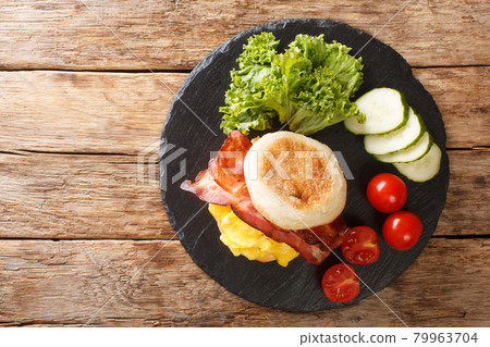 Closeup of a breakfast sandwich with scrambled eggs, bacon and cheese on an english muffin on a slate board. horizontal top view Closeup of a breakfast sandwich with scrambled eggs, bacon and cheese on an english muffin on a slate board. horizontal top view 79963704