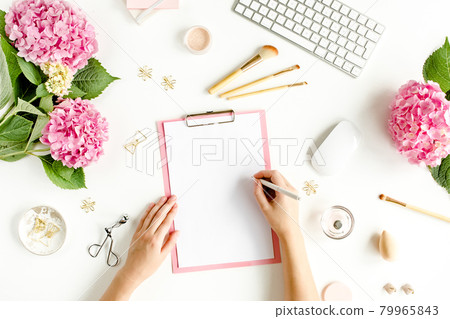 Female workspace with female hands, clipboard, bouquet hydrangea, computer, accessories on white background. Stylized women's desk. Flat lay. Top view 79965843