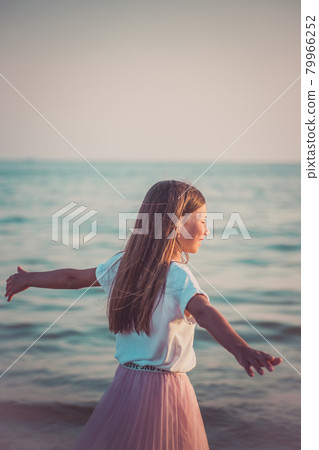 Happy little girl is spinning and dancing on the beach on a Sunny day. 79966252