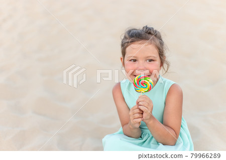 Cute little girl with big colorful lollipop. Child eating sweet candy bar. Sweets for young kids. Summer outdoor fun. Cute little girl with big colorful lollipop. Child eating sweet candy bar. Sweets for young kids. Summer outdoor fun. 79966289