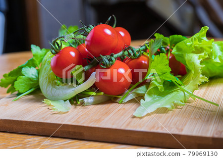 Fresh cherry tomatoes with green salad and garlic on a cutting board. 79969130