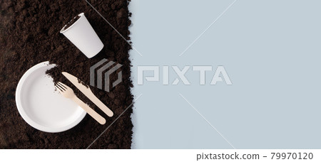 Paper plate and glass, wooden knife and fork on soil on blue flat lay composition, top view. Compostable or biodegradable dinnerware concept horizontal banner format with copy space Paper plate and glass, wooden knife and fork on soil on blue flat lay composition, top view. Compostable or biodegradable dinnerware concept horizontal banner format with copy space 79970120