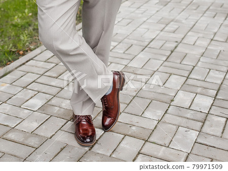 The man's legs are leg by foot in light trousers and brown shoes stand on paving tile The man's legs are leg by foot in light trousers and brown shoes stand on paving tile 79971509