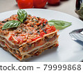 Piece of lasagna with basil leafs on white plate 79999868