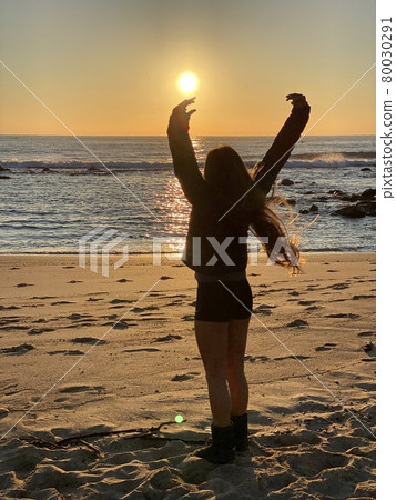 A girl banzai towards the rising sun on a sandy... - Stock Photo