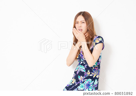 A young woman in a blue one-piece, making a sore throat gesture in front of a white wall 80031892