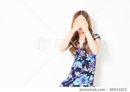 A young woman in a blue one-piece, hiding her face in front of a white wall 80031925