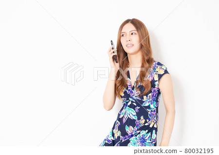 一位身穿藍色連衣裙的年輕女子在白牆前使用智能手機 一位身穿藍色連衣裙的年輕女子在白牆前使用智能手機 80032195
