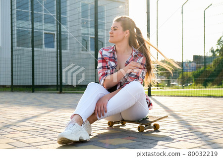 Young millennial woman hippie sitting on skateboard. Summer Skate Sessions. Woman cruising on a longboard in a park. Carefree female skater 20s enjoying freedom youth lifestyle Young millennial woman hippie sitting on skateboard. Summer Skate Sessions. Woman cruising on a longboard in a park. Carefree female skater 20s enjoying freedom youth lifestyle 80032219