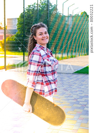 Cute millennial woman smile happy walking down the street with her skateboard. sun backlight and freedom rebel independent concept. Spending day for active board hobby Cute millennial woman smile happy walking down the street with her skateboard. sun backlight and freedom rebel independent concept. Spending day for active board hobby 80032221