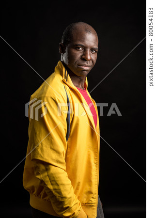 Side view of an African American man standing looking at camera black background 80054183