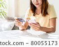 Young asian woman holding a credit card and using smart phone for make an online shopping payment at home 80055173
