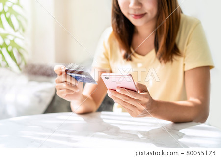 Young asian woman holding a credit card and using smart phone for make an online shopping payment at home Young asian woman holding a credit card and using smart phone for make an online shopping payment at home 80055173