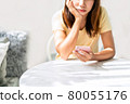 Bored young asian woman looking disappointed at her smart phone while waiting someone in restaurant 80055176