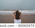 Young woman feeling lonely and sad looking at the sea on a gloomy day 80060979