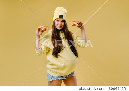 pregnant girl in yellow clothes with hamburgers in her hands on a yellow background 80064413